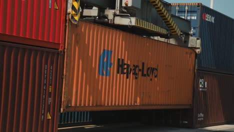 Container-crane-loading-orange-Hapag-Lloyd-container-onto-freight-train,-clear-daylight,-industrial-area