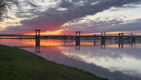 Der-Fluss-Loire-Fließt-Langsam-Unter-Einer-Alten-Brücke-Hindurch,-Im-Hintergrund-Der-Rote-Sonnenuntergang