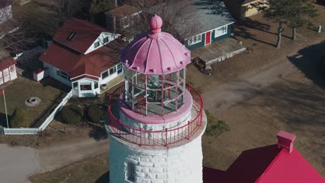 A-charming-lighthouse-with-a-pink-dome-on-a-sunny-day,-surrounded-by-small-buildings,-aerial-view