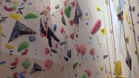 Mujer-Descendiendo-Colorido-Muro-De-Escalada-Interior,-Gimnasio-De-Escalada-En-Roca