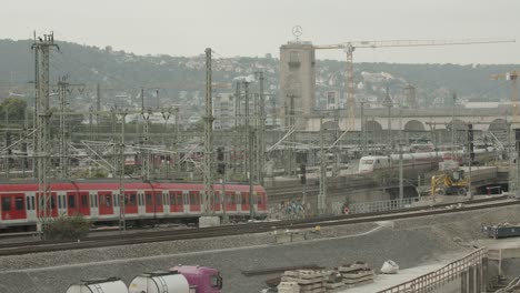 Estación-De-Ferrocarril-Con-Múltiples-Trenes-Y-Vías,-Telón-De-Fondo-Urbano-Con-Elementos-Industriales,-Cielo-Nublado