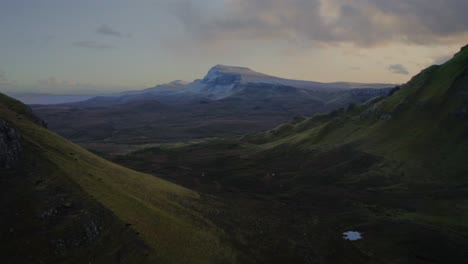 The-lush-green-highlands-on-the-Quiraing-Walk-and-a-distant-snowy-mountain,-Iske-of-Skye,-Scotland