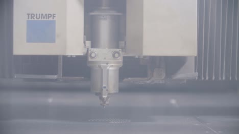 Industrieller-Laserschneider-In-Aktion,-Der-Komplizierte-Muster-Auf-Metall-Erzeugt,-Aufgenommen-In-Einer-Nebligen,-Blau-Getönten-Werkstatt