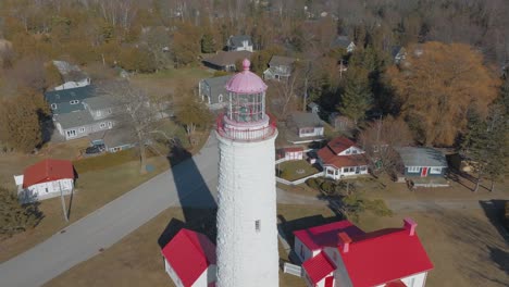 Ein-Bezaubernder-Leuchtturm-Mit-Einer-Rosa-Spitze,-Umgeben-Von-Malerischen-Häusern-Und-Blattlosen-Bäumen-In-Einem-Küstendorf,-Luftaufnahme