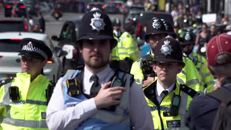 A-unit-of-Metropolitan-police-officers-wearing-fluorescent-yellow-jackets,-apart-from-a-liaison-officer-wearing-a-blue-tabard,-march-alongside-a-protest-during-a-public-order-incident