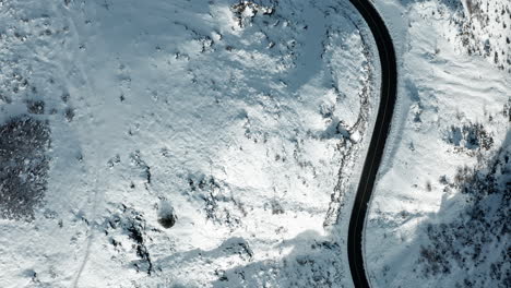 A-curvy-road-snaking-through-a-snow-covered-landscape,-offering-a-stark-contrast,-aerial-view