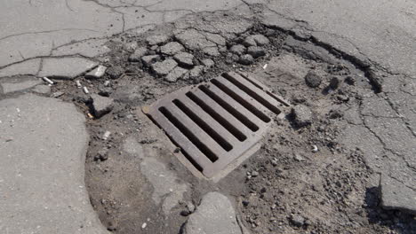 Broken-asphalt-around-rain-drain-manhole-in-city-street