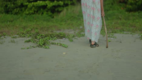 Woman-with-a-cane-walking-on-a-sandy-path-in-daylight,-close-up-on-feet