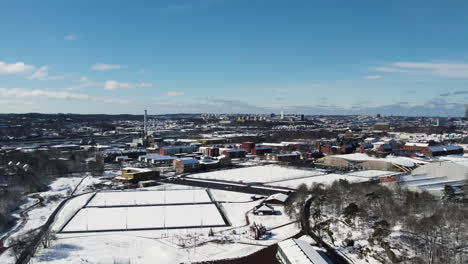Soccer-field-Covered-in-Snow-at-Kviberg-Park-and-Gothenburg-CItyscape-Background,-Aerial