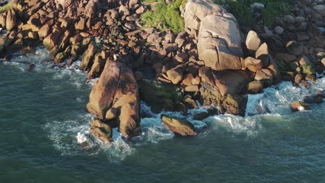 Landscape-of-waves-hitting-rocky-shoreline-of-tourist-district-Barra-Da-Lagoa,-Santa-Catarina,-Florianópolis,-Brazil