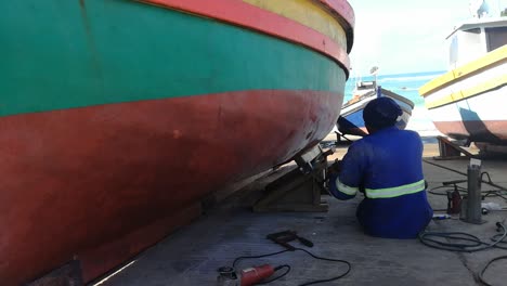 A-black-South-African-man-is-doing-repair-work-on-a-grounded-fishing-boat-in-the-harbour-at-Arniston