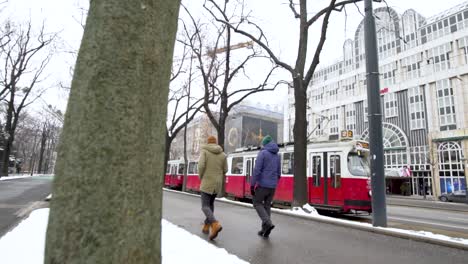 Dolly-shot-of-men-walking-Vienna-street-in-Winter-with-red-tram-passing-by,-Austria