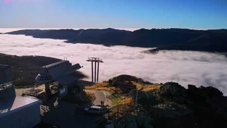 Aerial-of-ski-chairlift-at-Thredbo-overlooking-cloudy-foggy-valley-during-summer-in-Snowy-Mountains,-NSW,-Australia