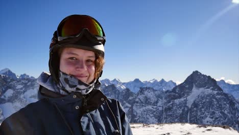 woman-in-ski-clothes-smiling-at-the-camera-with-mountain-view,-on-a-sunny-day