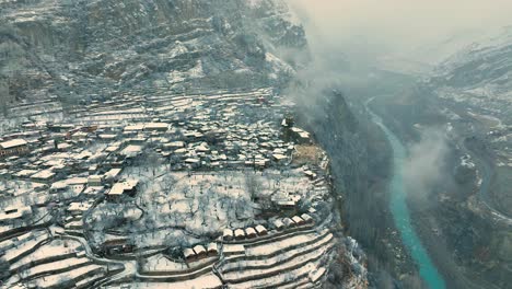 Vista-Aérea-De-Karimabad-Cubierto-De-Nieve-En-Lo-Alto-De-Un-Acantilado-Junto-Al-Río