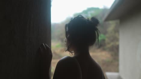 Silhouetted-young-woman-gazing-out-a-window-in-a-dimly-lit-room,-evoking-a-sense-of-contemplation-and-solitude