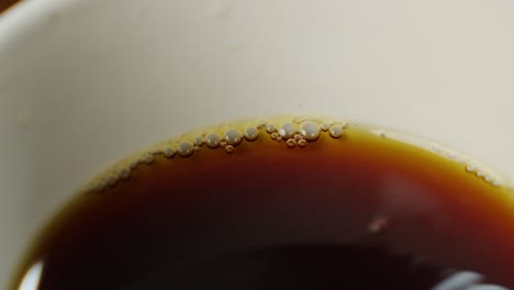 Extreme-Nahaufnahme-Von-Schwarzem-Kaffee-In-Einer-Weißen-Tasse,-Detailaufnahme-Kleiner-Bläschen-Auf-Der-Oberseite