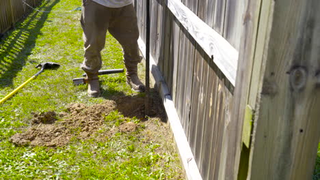 Man-using-a-prybar-to-dig-out-a-post-hole