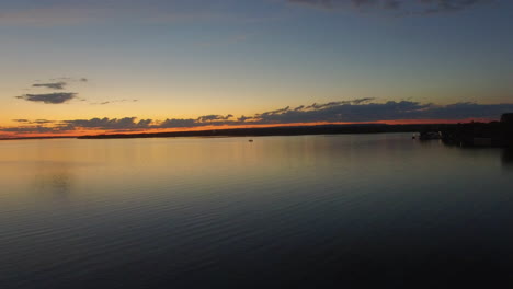 A-boat-travels-across-a-calm-lake-as-the-sunset-leaves-an-orange-glow-along-the-horizon