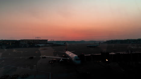 Time-lapse-of-the-sunset-inside-an-airport-where-the-planes-are-being-unloaded-with-luggage