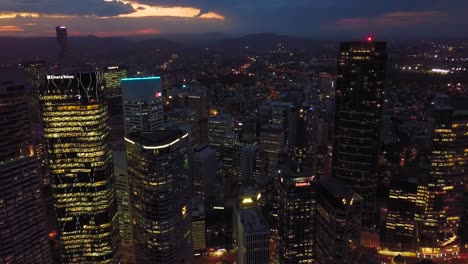 Aerial-view-of-a-modern-city-center-with-tall-buildings,-lights-and-dramatic-clouds-in-the-evening