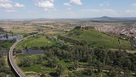 Aerial-drone-sweeps-over-Medellín,-Badajoz,-revealing-its-ancient-castle,-meandering-river,-and-picturesque-landscape