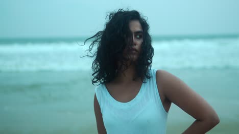 Woman-standing-confidently-on-a-beach-with-windswept-hair-and-a-serious-expression,-overcast-day,-close-up