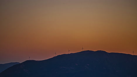 Silhouette-of-wind-turbines-generating-energy-on-top-of-mountain,-distance-time-lapse-view