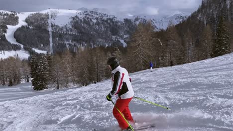 Follow-shot-of-a-person-who-is-learning-to-do-slalom-on-skis-on-the-ski-slope-right-next-to-the-ski-lift-and-with-mountains-and-the-woods-in-the-background