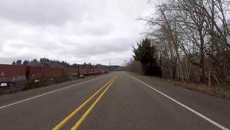 Driving-down-the-road-next-to-a-graffiti-covered-train-sitting-next-to-a-river-in-Oregon