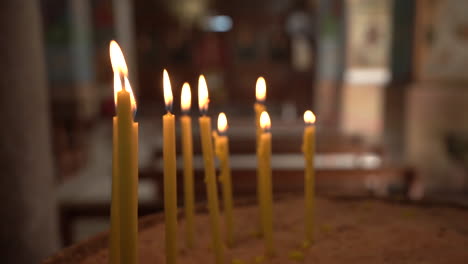A-Set-Of-Yellow-Burning-Candle-Sticks-With-Thrown-Out-of-Focus-Madaba-St-George's-Greek-Orthodox-Church-Background,-100-Frames-Per-Second