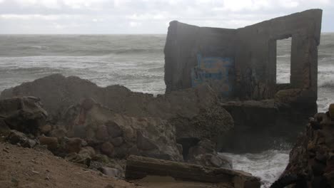 Big-waves-hitting-the-abandoned-concrete-coast-defense-building-ruins-with-graffiti-in-stormy-weather