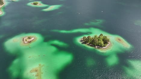 Eibsee's-emerald-green-waters-highlighting-small,-forested-islands-and-sandy-shallows-in-Grainau,-Germany---aerial