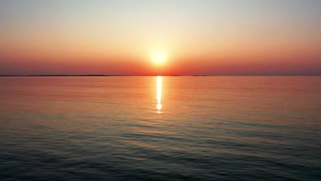 Wunderschöner-Sonnenuntergang-Am-Meer-Mit-Hell-Leuchtender-Sonne,-Die-Farbenfrohe-Rote,-Orange,-Violette-Und-Gelbe-Reflexe-Auf-Friedliche,-Plätschernde-Wellen-Des-Meeres-Wirft