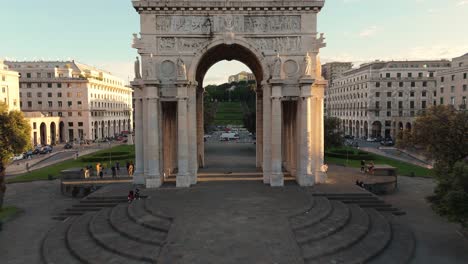 The-iconic-piazza-della-vittoria-in-genoa-during-sunset,-showcasing-the-grand-arch-and-bustling-cityscape,-aerial-view