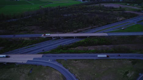 Luftaufnahme-Eines-Autobahnkreuzes-Mit-Sattelschleppern,-Die-In-Der-Dämmerung-Fahren