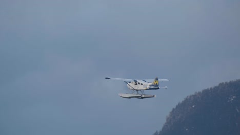 A-Flying-Boat-Soaring-High-Over-Brockton-Point,-Stanley-Park-In-Vancouver,-British-Columbia-With-Majestic-Mountains-In-The-Background---panning-shot