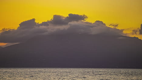 Silhouettes-of-rugged-cliffs-with-clouds-in-time-lapse-as-sky-blazes-with-fiery-hues