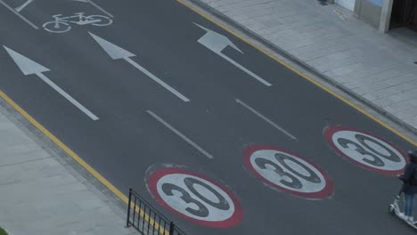 High-angle-of-road-with-painted-speed-limit-road-signs,-cars-and-scooter-driving-in-Lugo,-Spain