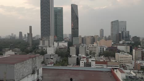 Eine-Person-Auf-Einem-Dach-Beobachtet-Die-Wolkenkratzer-Von-Mexiko-Stadt,-Während-Eine-Drohne-In-Die-Ferne-Fliegt