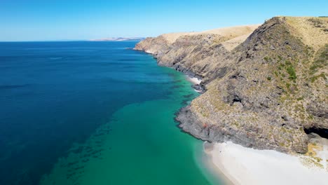 A-drone-shot-flying-backwards-which-reveals-a-beautiful-white-sand-beach-surrounded-by-tall-hills-and-rock-formations