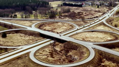 Aerial-drone-slow-fly-roundabout-highway-road-in-Latvia-countryside-Valmeiras-Traffic-panoramic-wide-landscape,-dry-fields,-town-background