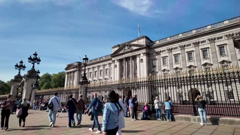 People-stroll-in-front-of-Buckingham-Palace-on-a-sunny-morning-in-London,-England,-with-the-vibrancy-of-city-life-and-the-allure-of-iconic-landmarks