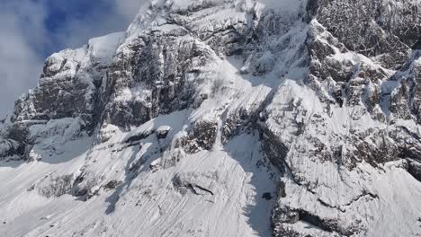 Vista-Aérea-De-Los-Escarpados-Acantilados-Cubiertos-De-Nieve-De-Fronalpstock-Bajo-Un-Cielo-Parcialmente-Nublado-En-Glarus-Nord,-Suiza