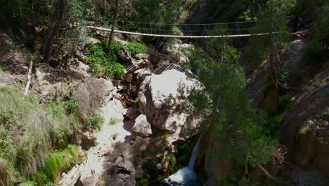 Hanging-wooden-walkway-over-a-mountain-stream-and-waterfall-with-colorful-turquoise-waters