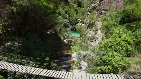 Hanging-wooden-walkway-over-a-mountain-stream-with-colorful-turquoise-waters