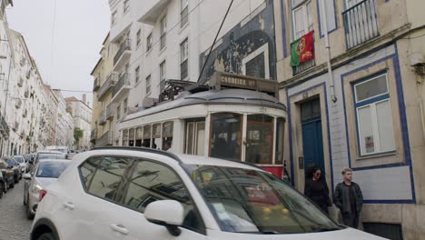 Aufnahme-Einer-Straßenbahn,-Die-Durch-Die-Stadt-Lissabon-Fährt,-Mit-Einer-Portugiesischen-Flagge,-Die-Am-Fenster-Eines-Hauses-In-Portugal-Weht