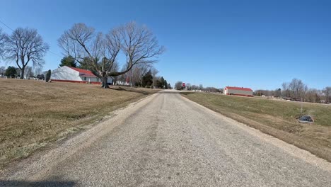 POV:-Conduciendo-Por-Una-Carretera-Rural-Pasando-Por-Un-Cementerio,-Un-Granero-Y-Campos-Vacíos-A-Principios-De-La-Primavera-En-El-Medio-Oeste