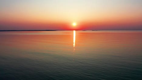 Beautiful-Ocean-Sunset-with-Bright-Glowing-Sun-Casting-Colorful-Red,-Orange,-Purple-and-Yellow-Reflections-Over-Peaceful-Rippling-Waves-of-the-Sea