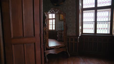 Small-Library-in-Trakošćan-Castle-,-Croatia,-featuring-an-ornate-wooden-mirror-and-stained-glass-windows